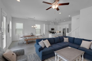 A modern living room with a blue sectional sofa, a wooden coffee table, and a dining area with a bench.