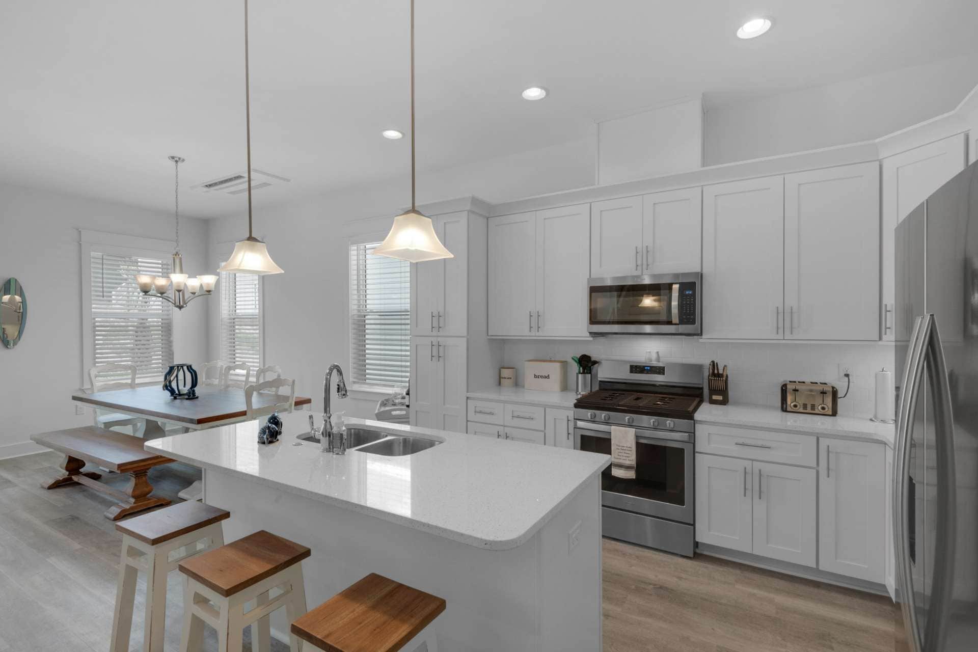 A modern kitchen with white cabinetry, a central island with stools, a stainless steel oven, and a microwave.