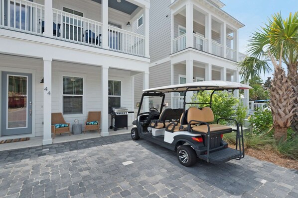A golf cart parked in front of a two-story building with a balcony and a patio area.