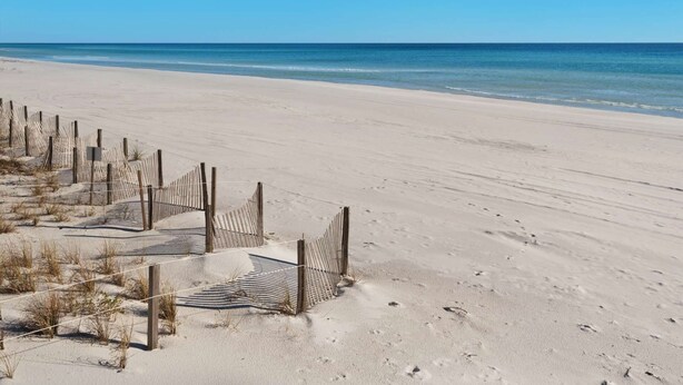 Ein Sandstrand mit Holzzaun und einem Schild.