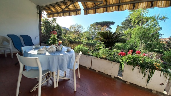 A covered outdoor dining area with a round table set for four, surrounded by white chairs.