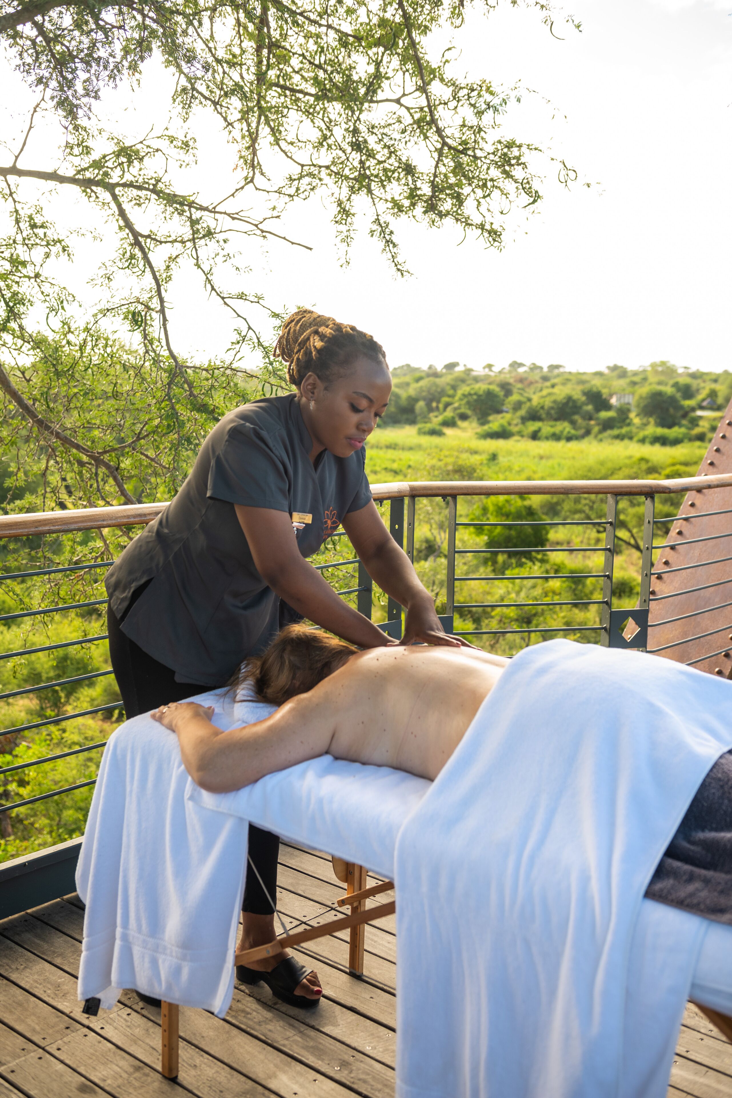 A massage therapy session on a wooden deck with a view of a lush green landscape.