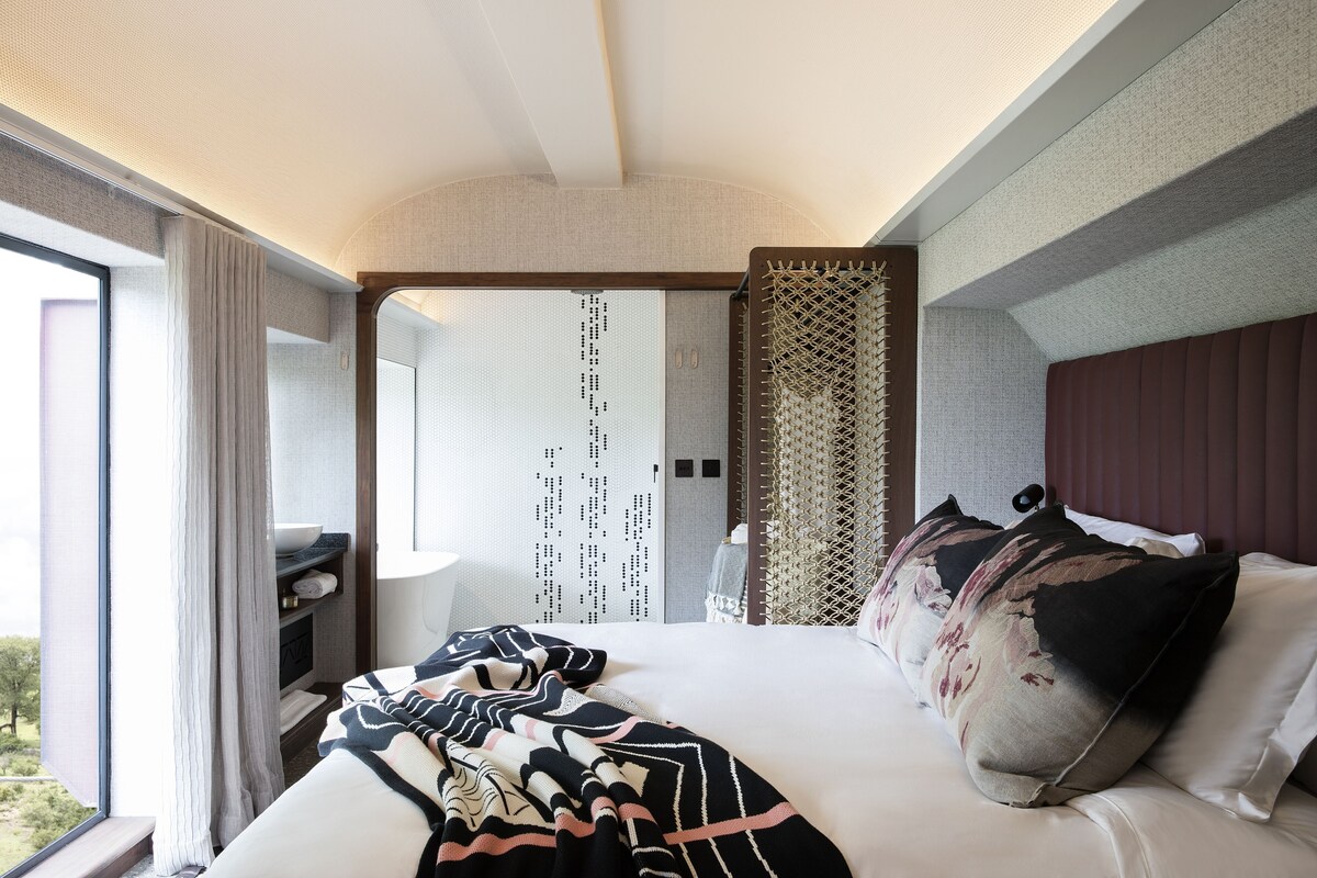 Een moderne hotelkamer met een groot bed, uitzicht op de natuur, een klein bureau en een raam met gordijnen.