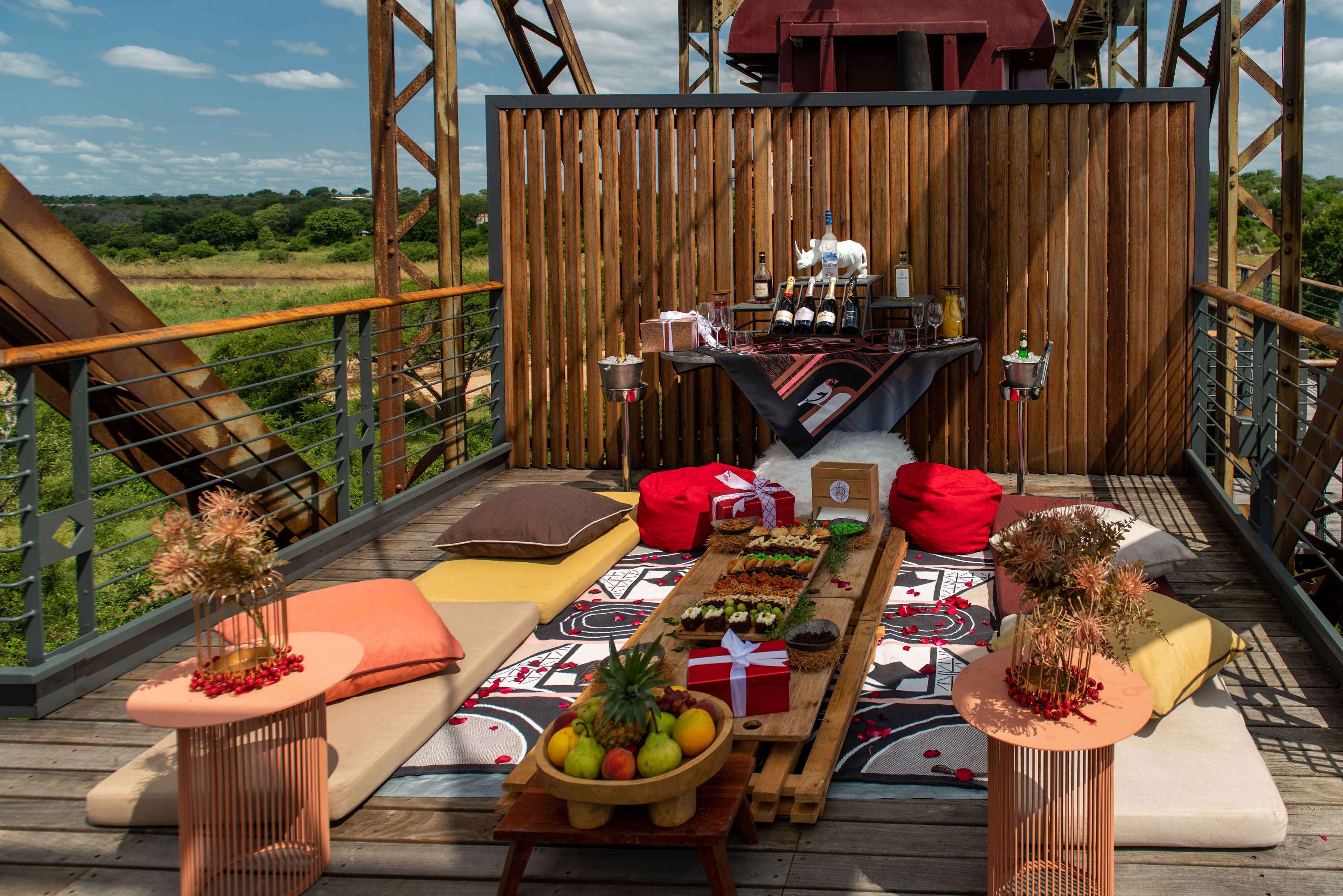 A wooden deck with a picnic setup, including a table with food, drinks, and a decorative centerpiece.