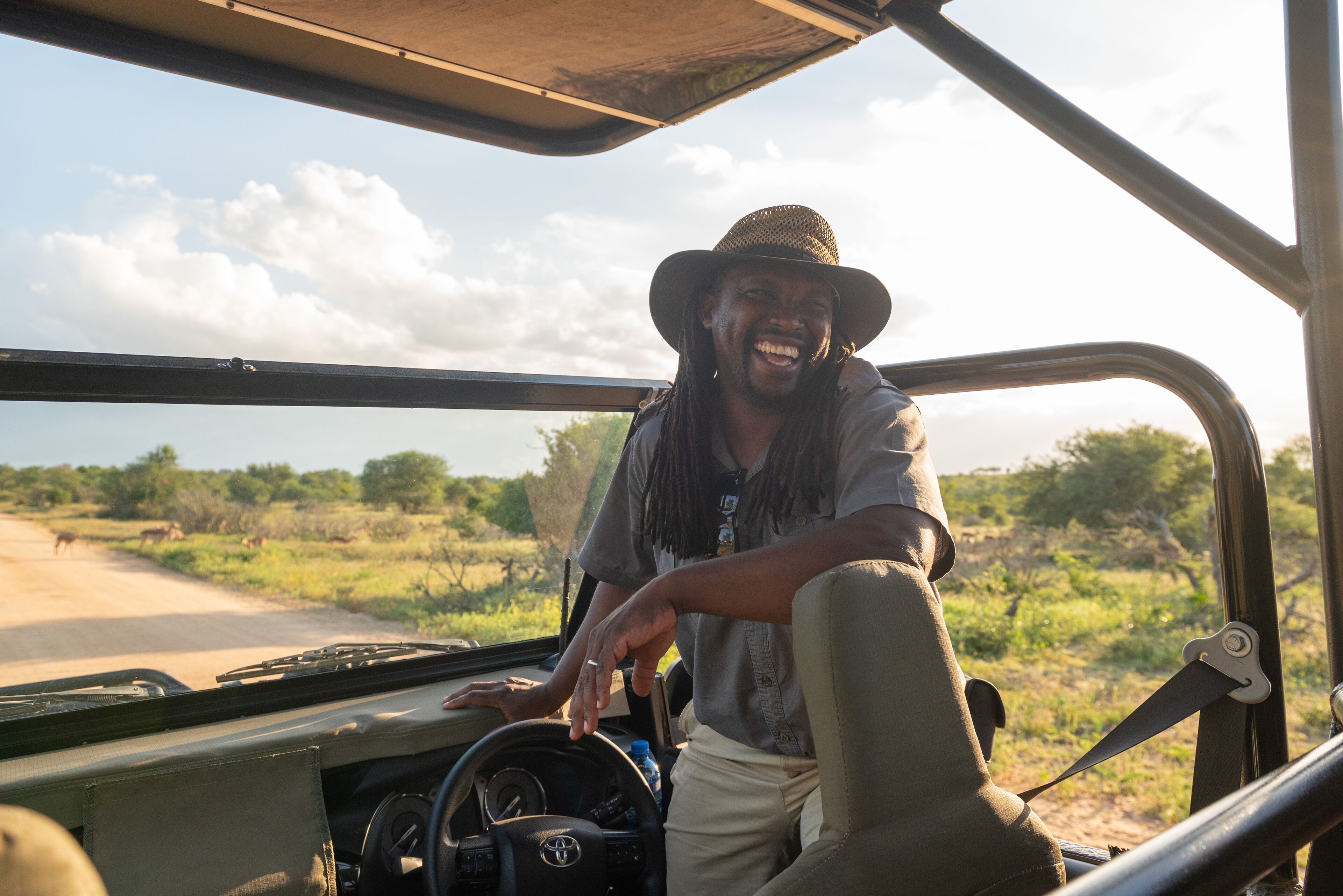A safari vehicle interior with a steering wheel, dashboard, and a person wearing a hat.