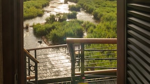 Une vue depuis un balcon donnant sur une rivière, avec une terrasse en bois et une rambarde en métal.