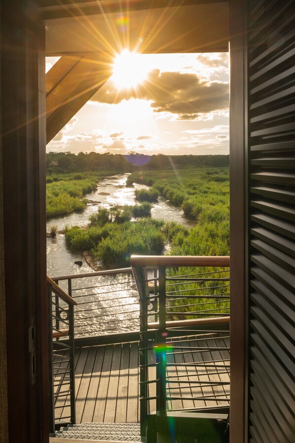 Uitzicht vanaf een balkon op een rivier, met een houten terras en een metalen hekwerk.