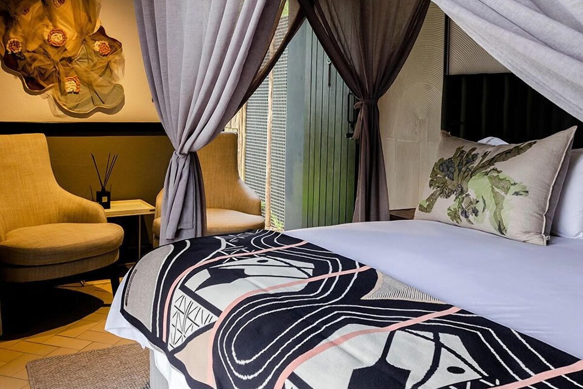 Een slaapkamer met een bed, een stoel, een nachtkastje en een kunstwerk aan de muur.
