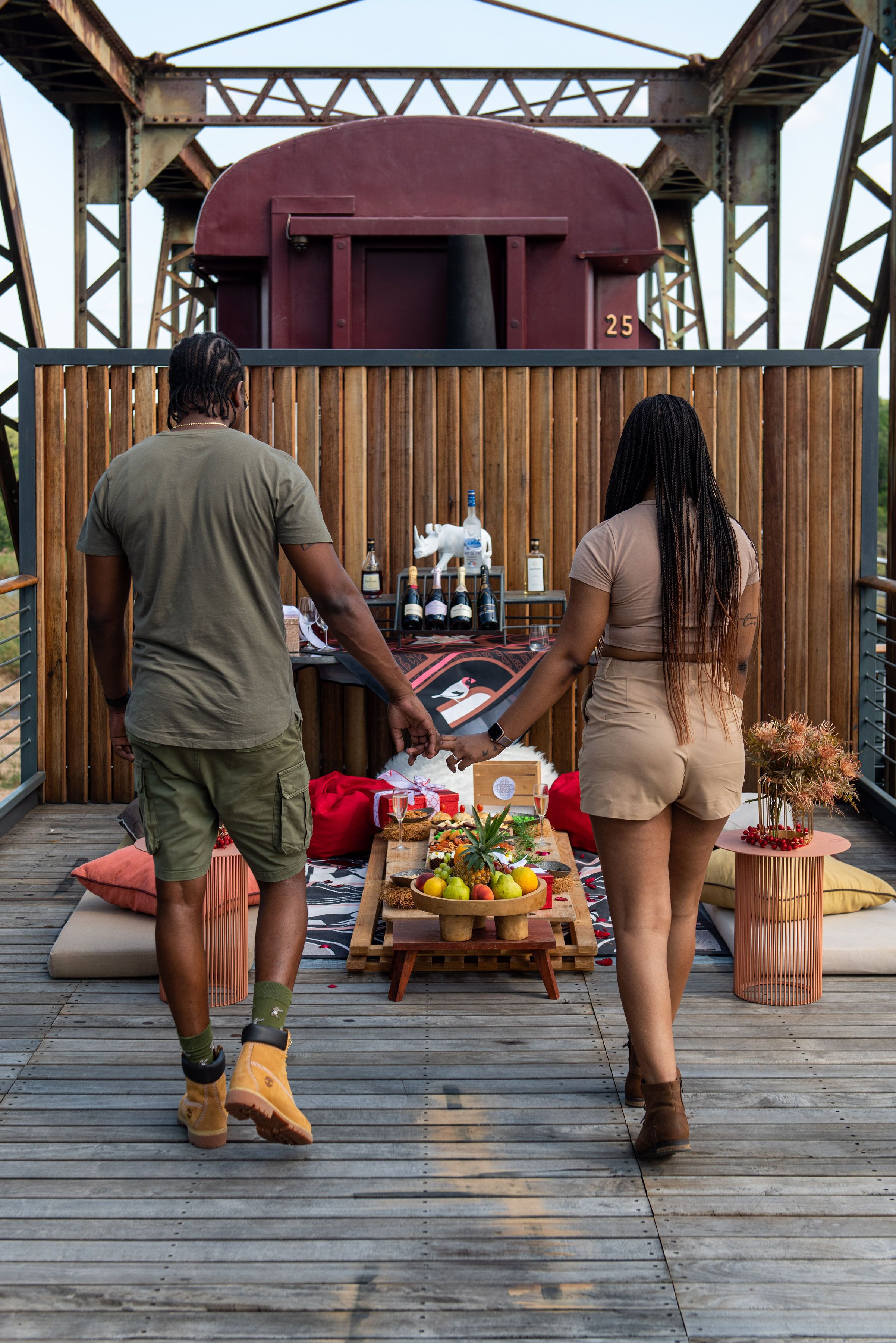 A wooden deck with a picnic setup, a red train car in the background, and a metal structure.