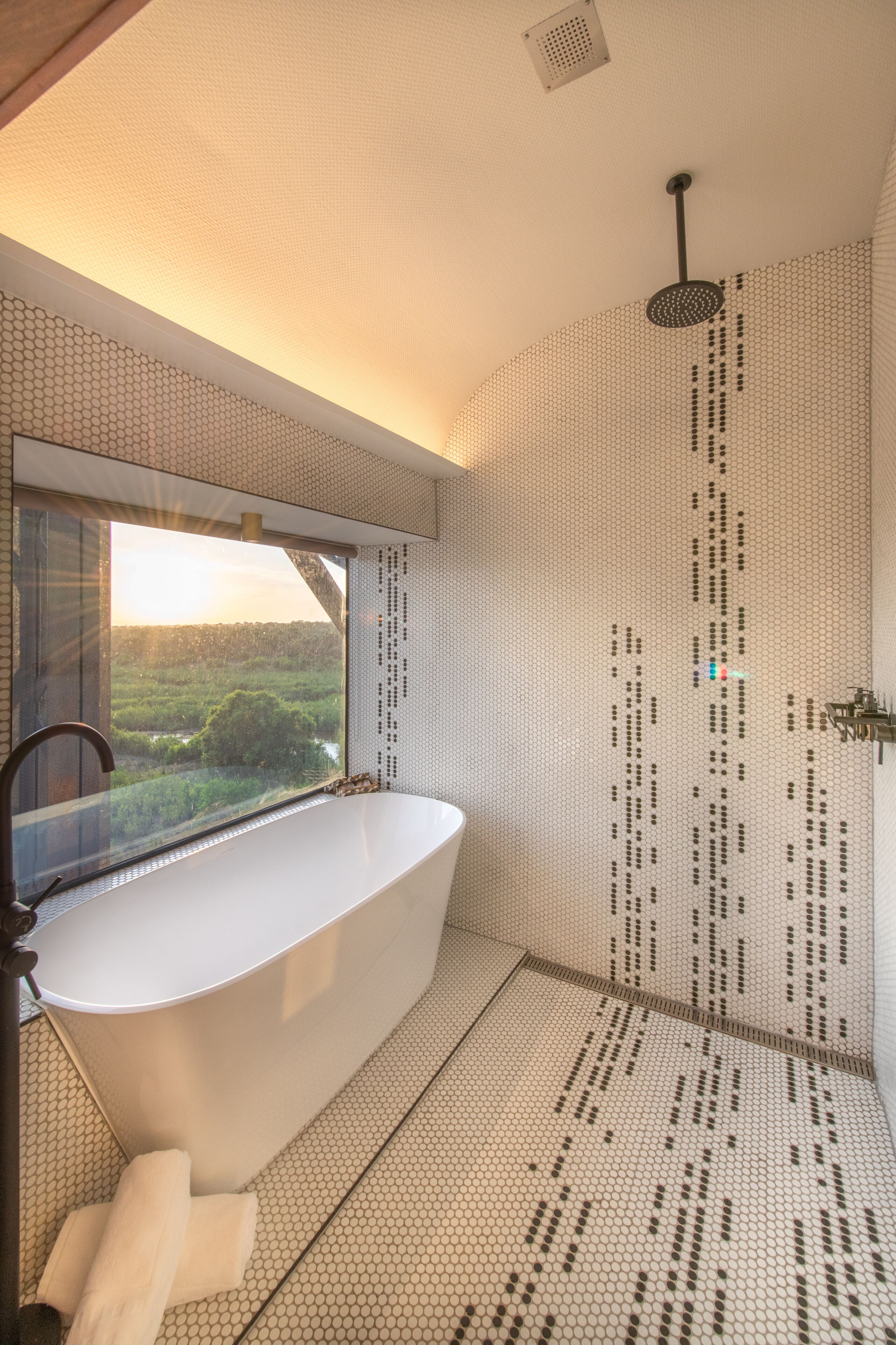 A modern bathroom with a freestanding bathtub, a showerhead, and a view of a lush landscape through a large window.