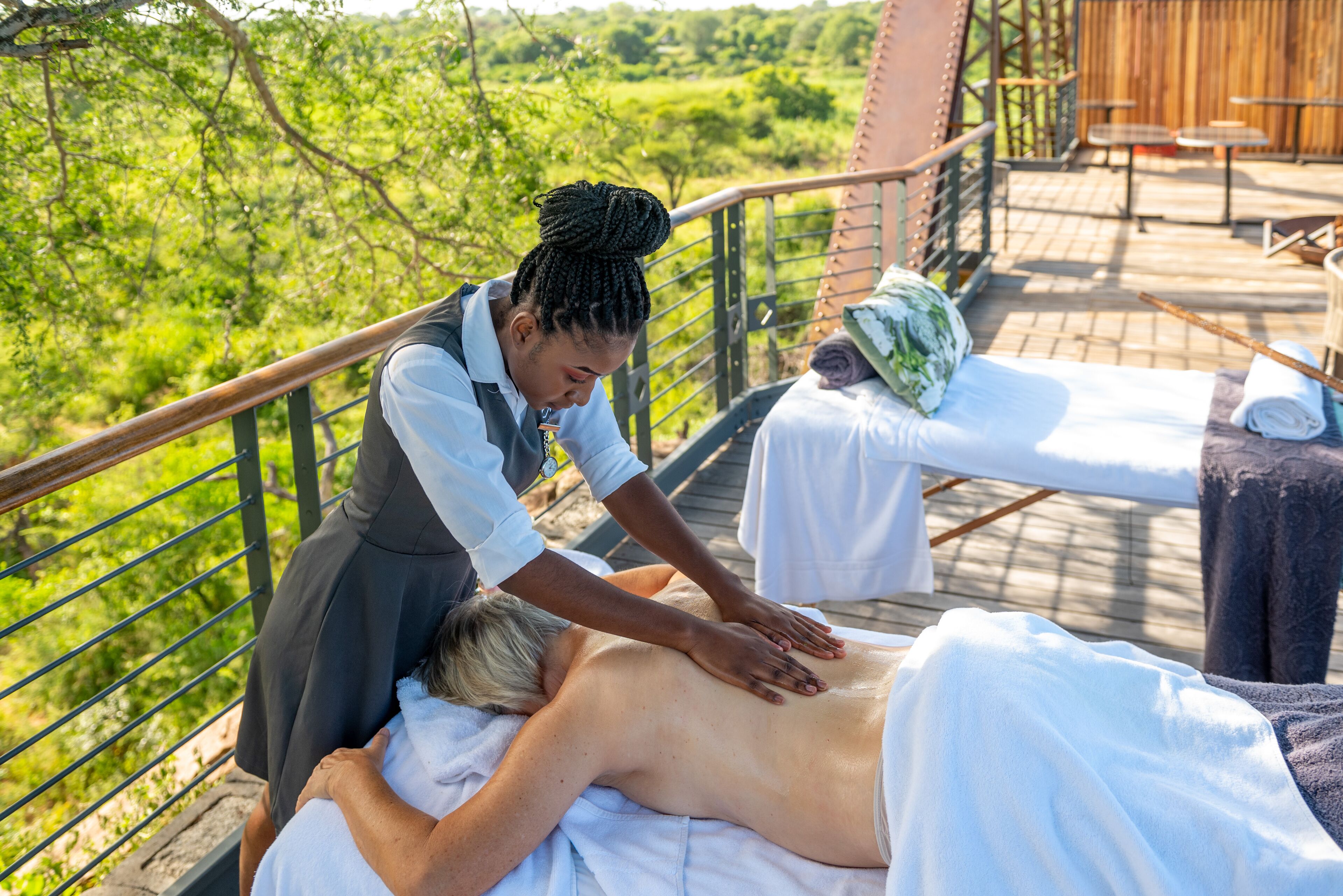 A massage therapy session on a wooden deck with a scenic view of greenery.