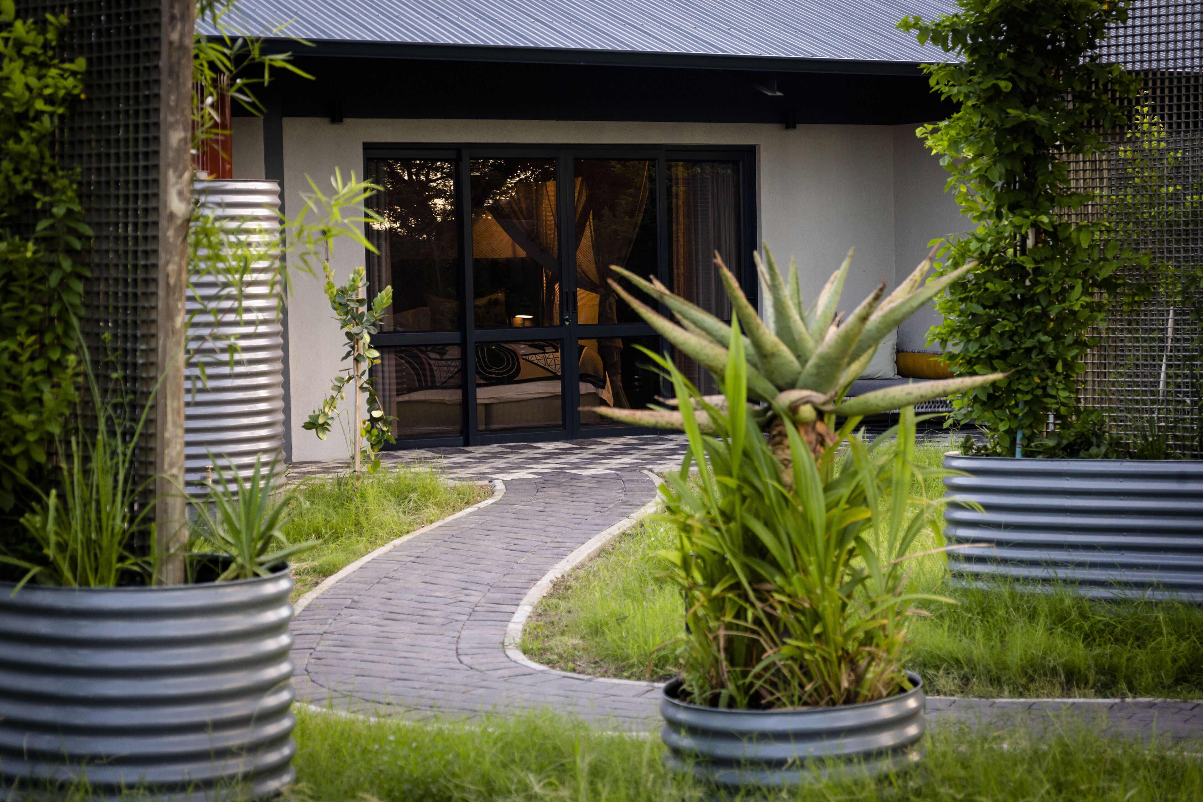 A pathway leading to a building with a modern design, featuring a glass door entrance and a covered outdoor seating area.