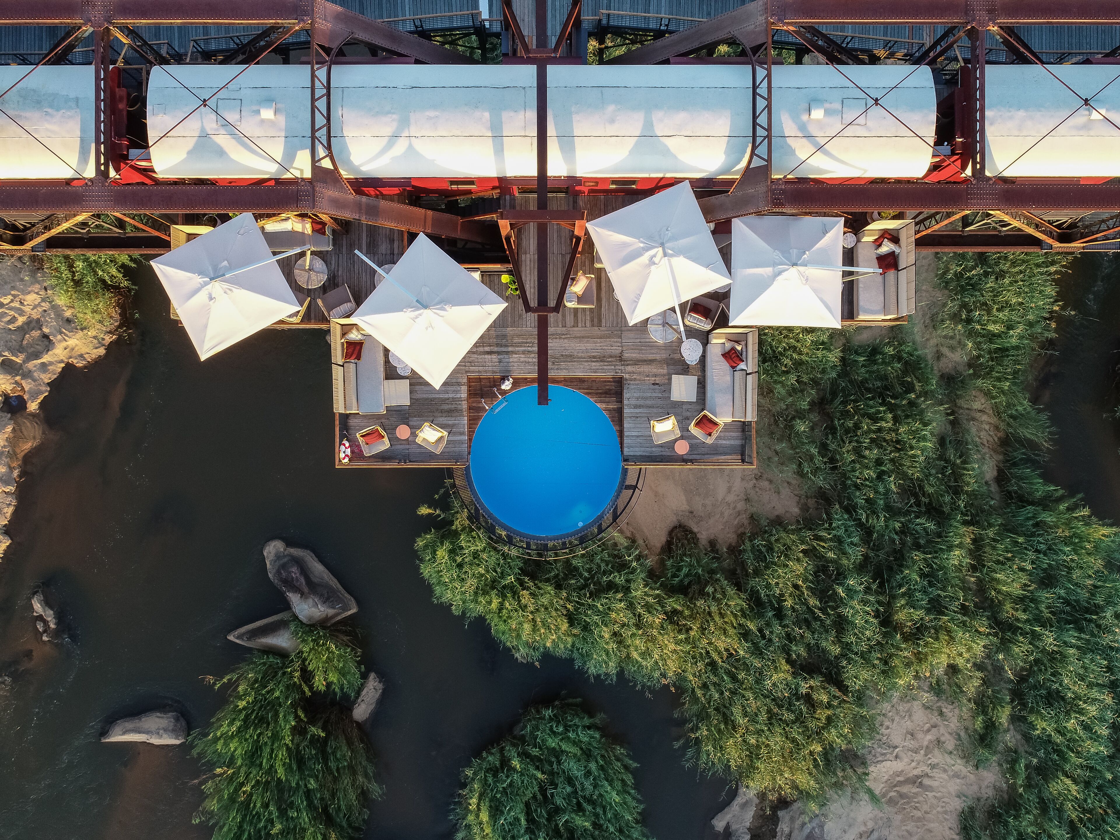 An aerial view of a rooftop pool area with a blue pool, white umbrellas, and outdoor furniture.