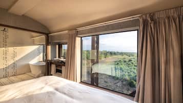 Habitación de hotel con una cama grande, baño con ducha y un amplio ventanal con vistas al campo.