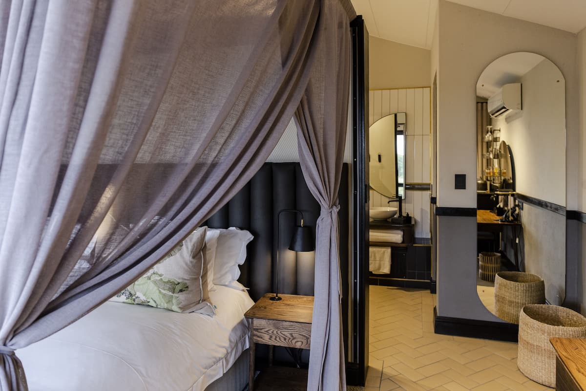 Une chambre à coucher avec un lit à baldaquin, une table de chevet, une lampe, un miroir et une armoire.