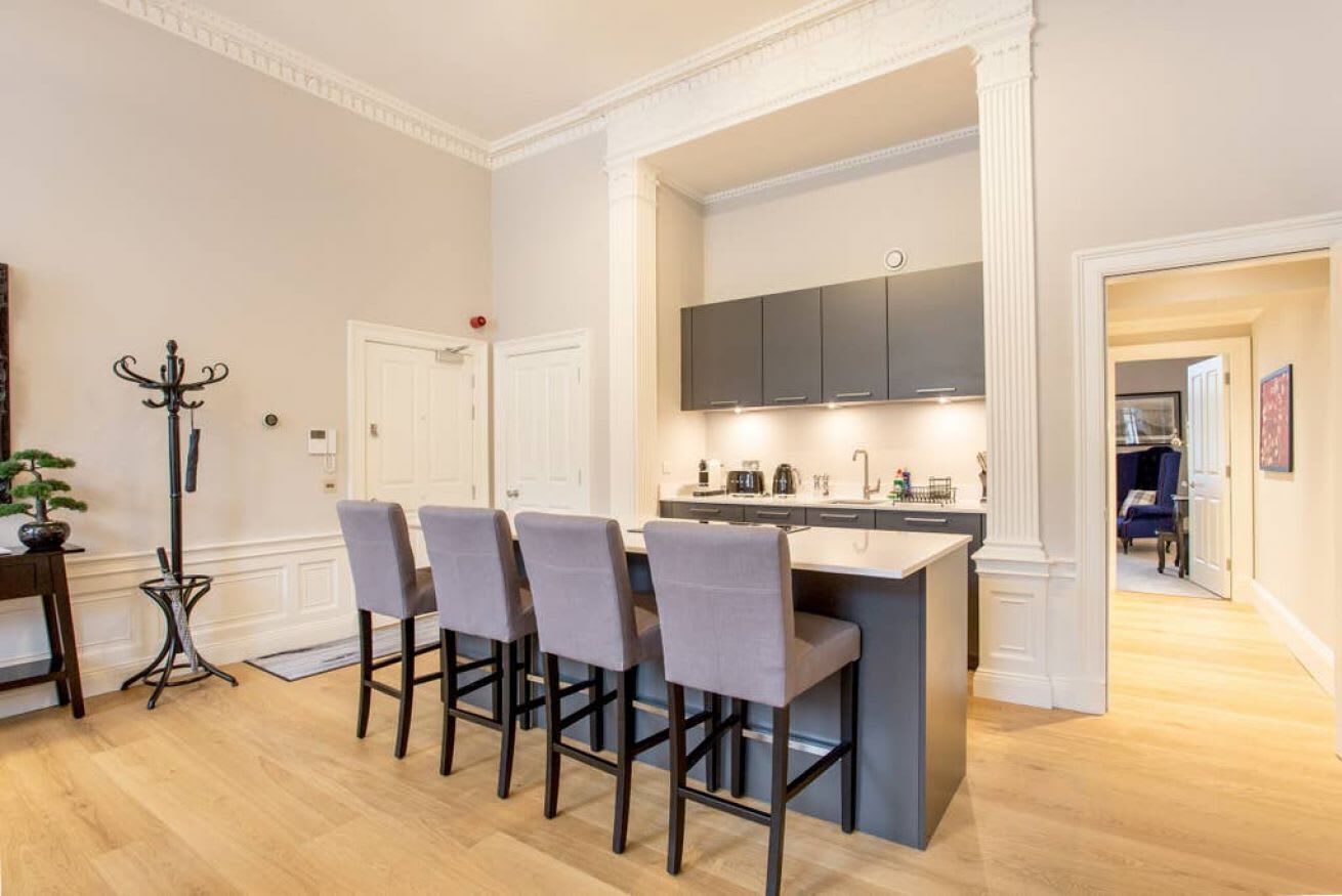 A modern kitchen with a central island, bar stools, and a dining area with a table and chairs.