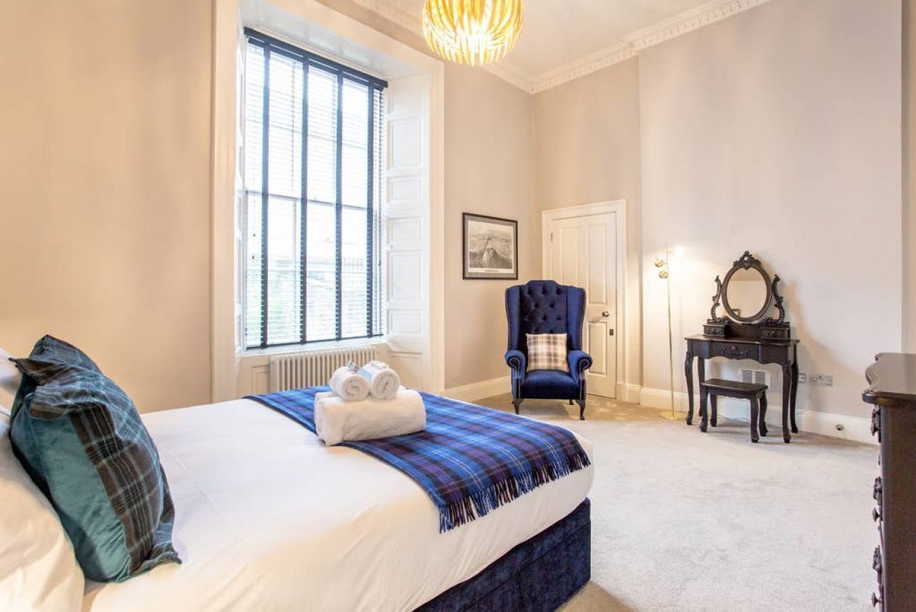 A bedroom with a large bed, a window, a chair, a dresser, and a mirror.