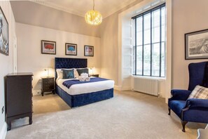 A bedroom with a large bed, bedside lamps, a dresser, a chair, and framed pictures on the wall. - Exquisite Flat in the City Centre (Edinburgh)