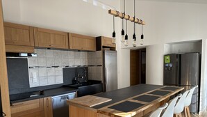 Cozinha moderna com armários de madeira, uma ilha grande com banquetas, uma geladeira de aço inoxidável e bancada preta.