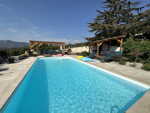 A rectangular swimming pool with clear blue water, surrounded by lounge chairs and umbrellas.