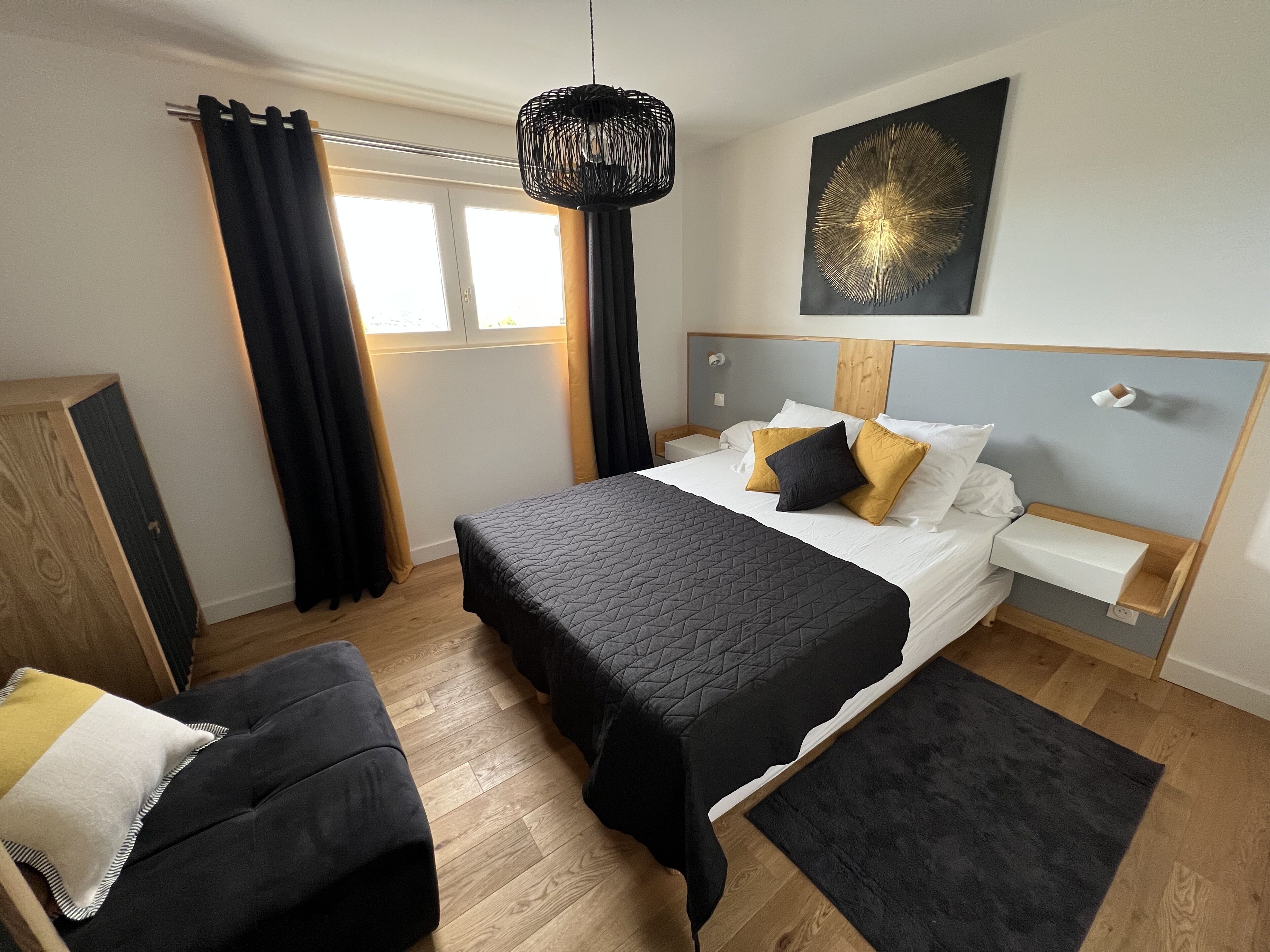 Ein modernes Schlafzimmer mit einem großen Bett, einem Nachttisch, einem Sessel, einem Fenster mit Vorhängen und einem Wandbild.