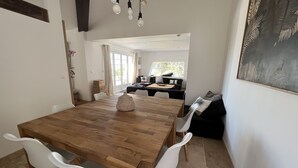 Uma sala de jantar com uma mesa de madeira e cadeiras brancas, um sofá e um quadro na parede.