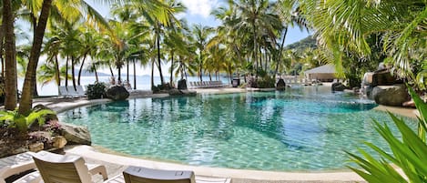 A pool area with lounge chairs and palm trees, surrounded by a natural landscape.