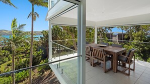 A modern outdoor dining area with a glass balustrade overlooking a lush landscape and a body of water. - Oasis 17 (Whitsundays)