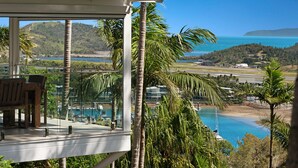 A balcony with a view of a coastal landscape, including a beach, a body of water, and a hilly background. - Oasis 17 (Whitsundays)