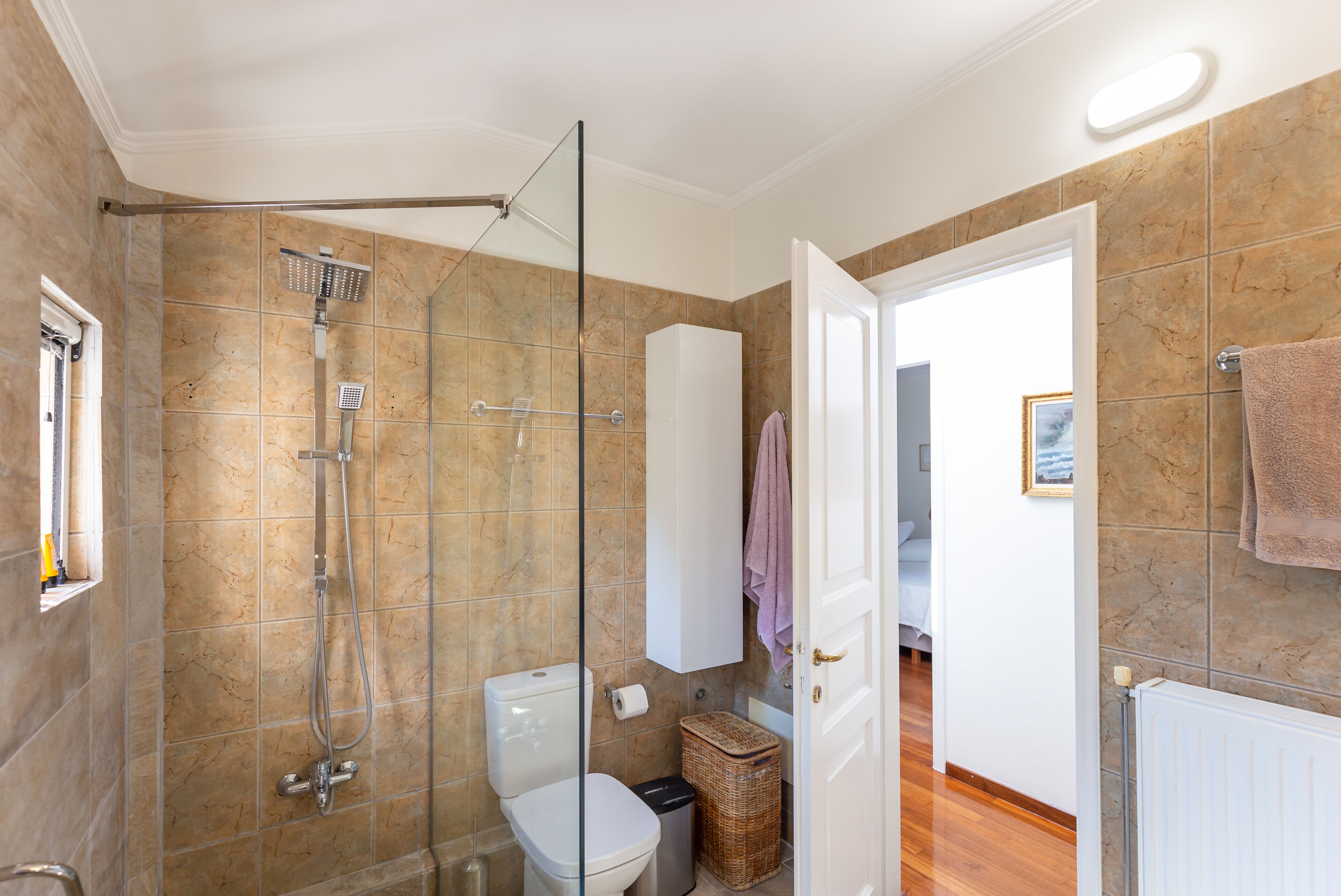 Une salle de bain avec une douche à parois de verre, des toilettes et une petite poubelle.