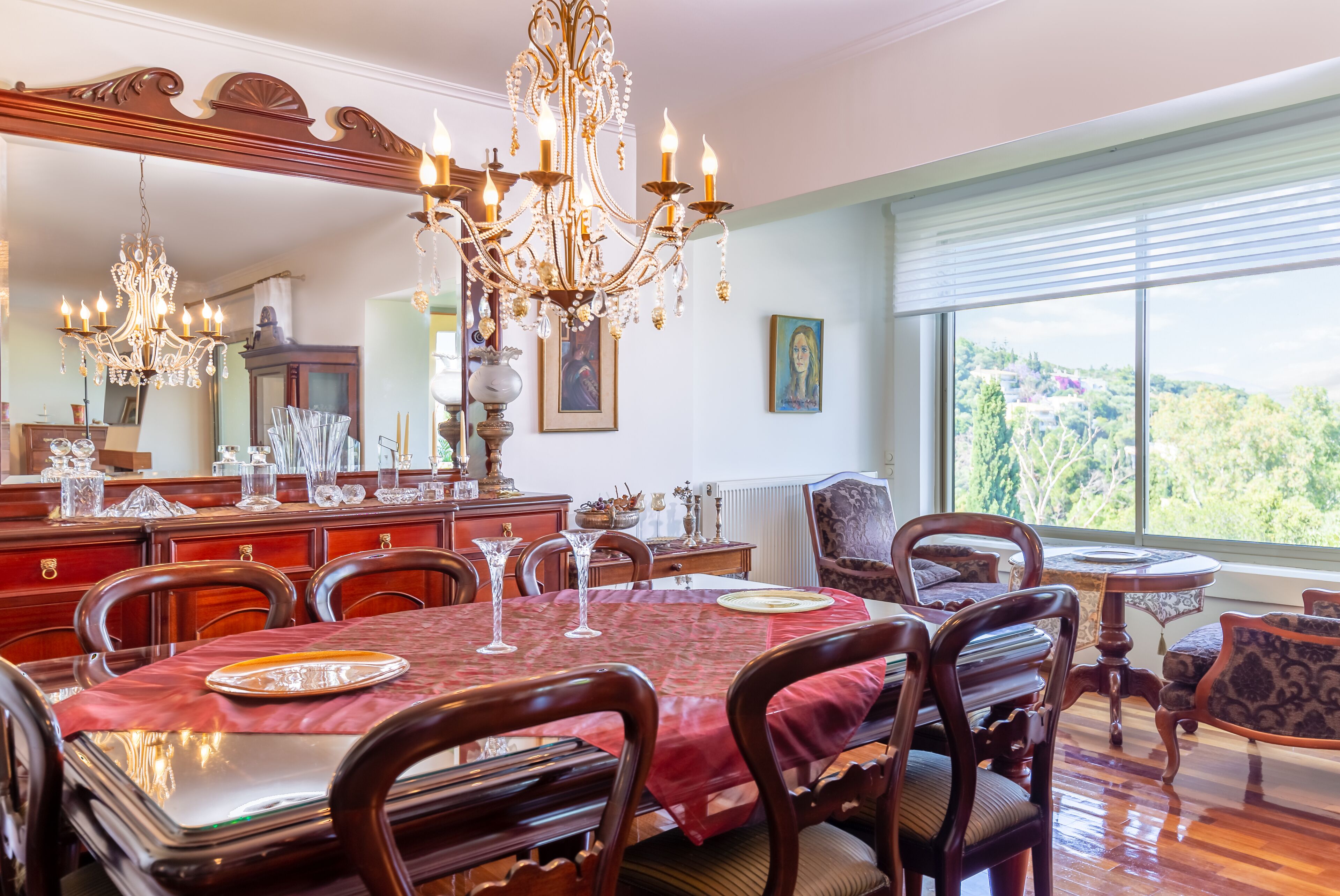Une salle à manger agrémentée d’un lustre, de meubles en bois et d’une grande fenêtre offrant une vue dégagée.