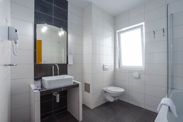 A modern bathroom with a white sink, dark tiles, a toilet, and a glass shower enclosure. - Villa Sv Kriz (Trogir)