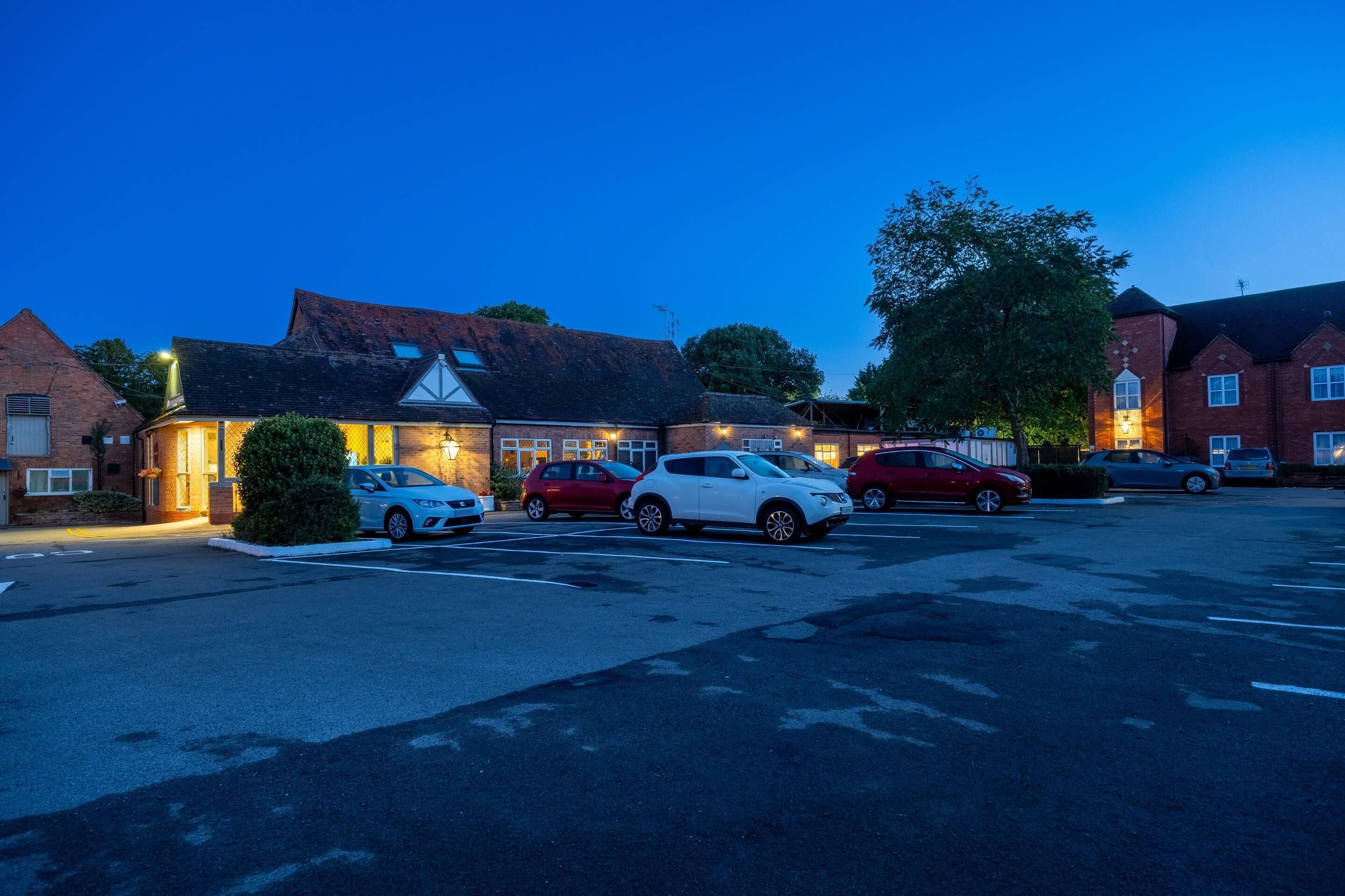 A parking lot with several cars parked in front of a building with a brick facade and a sloped roof.