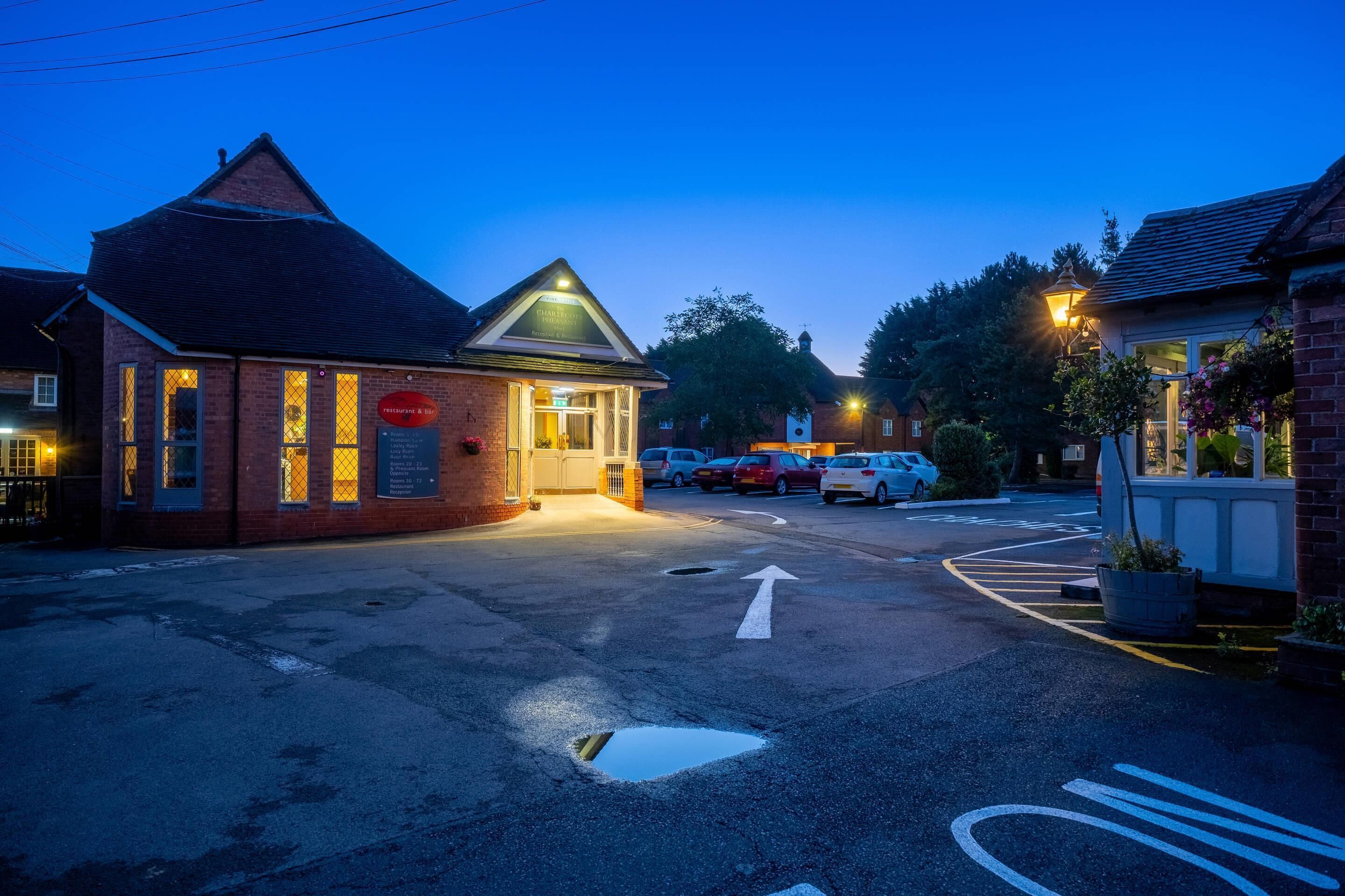 A building with a sign that reads "CHARTERHOUSE HOTEL" and a parking lot with cars.