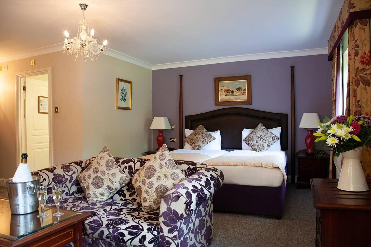 Quarto com cama, sofá, lustre e um vaso com flores.