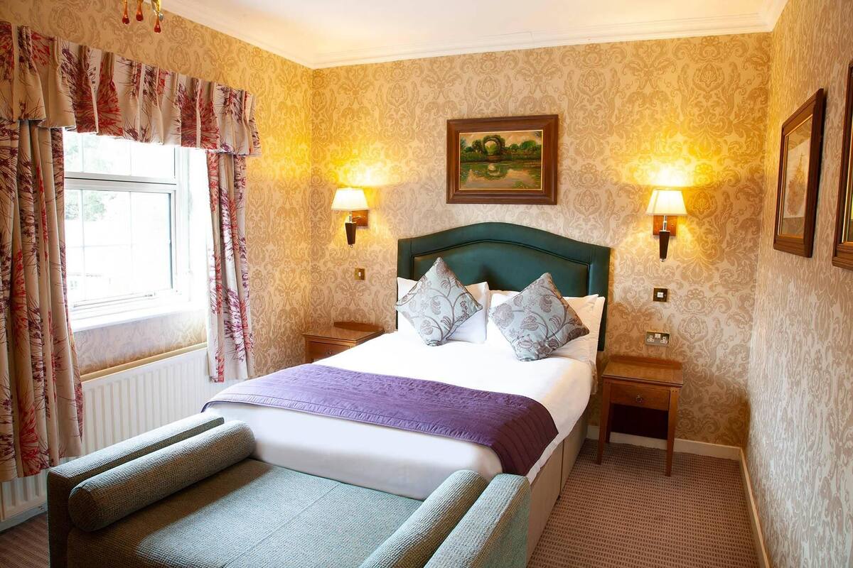 Quarto de hotel com uma cama grande, duas mesas de cabeceira, uma cabeceira e uma janela com cortinas.