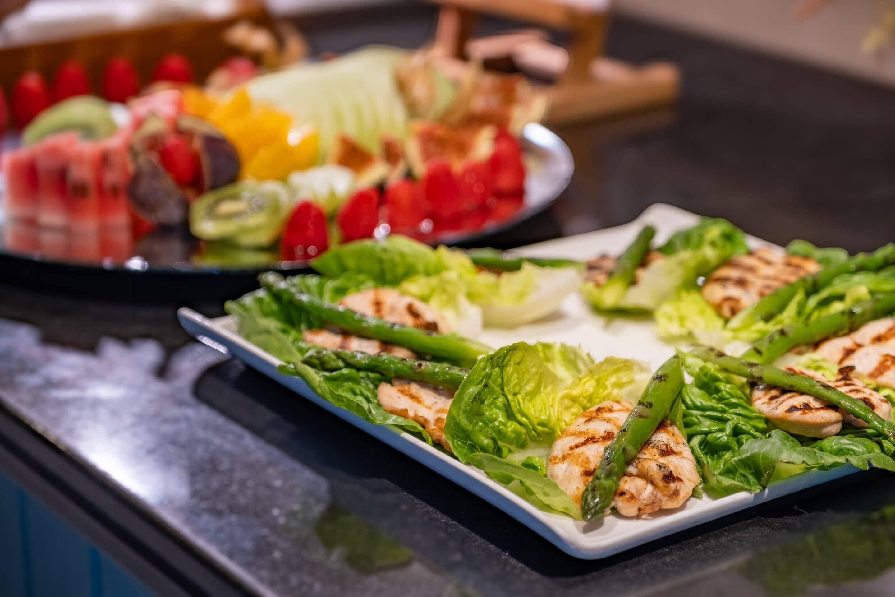 Ein reichhaltiges Buffet mit verschiedenen Speisen, darunter gegrilltem Hähnchen, Spargel und gemischten Früchten.