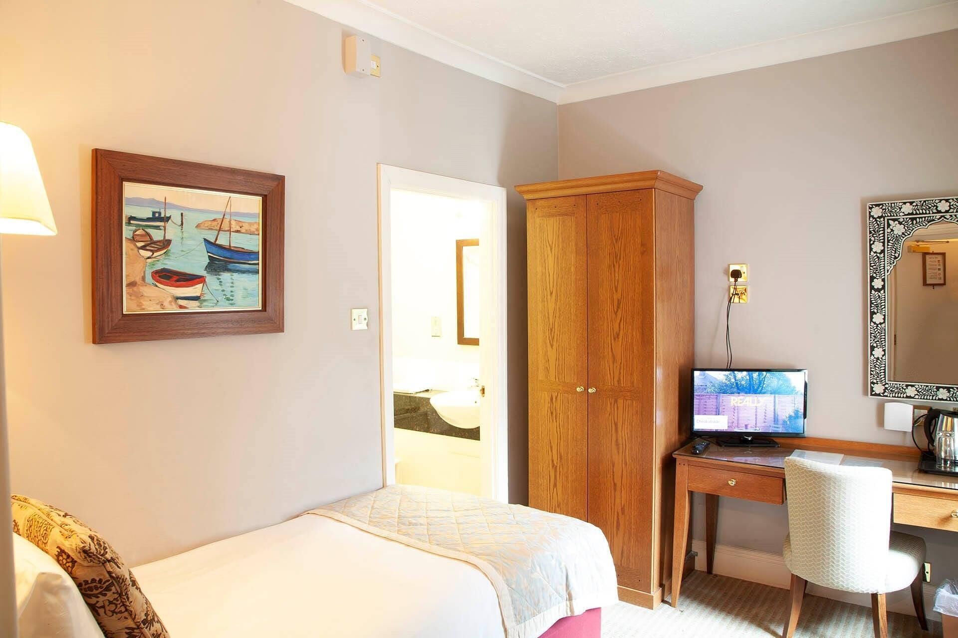Une chambre d ’hôtel avec un lit, un bureau avec un ordinateur, une armoire et un tableau au mur.