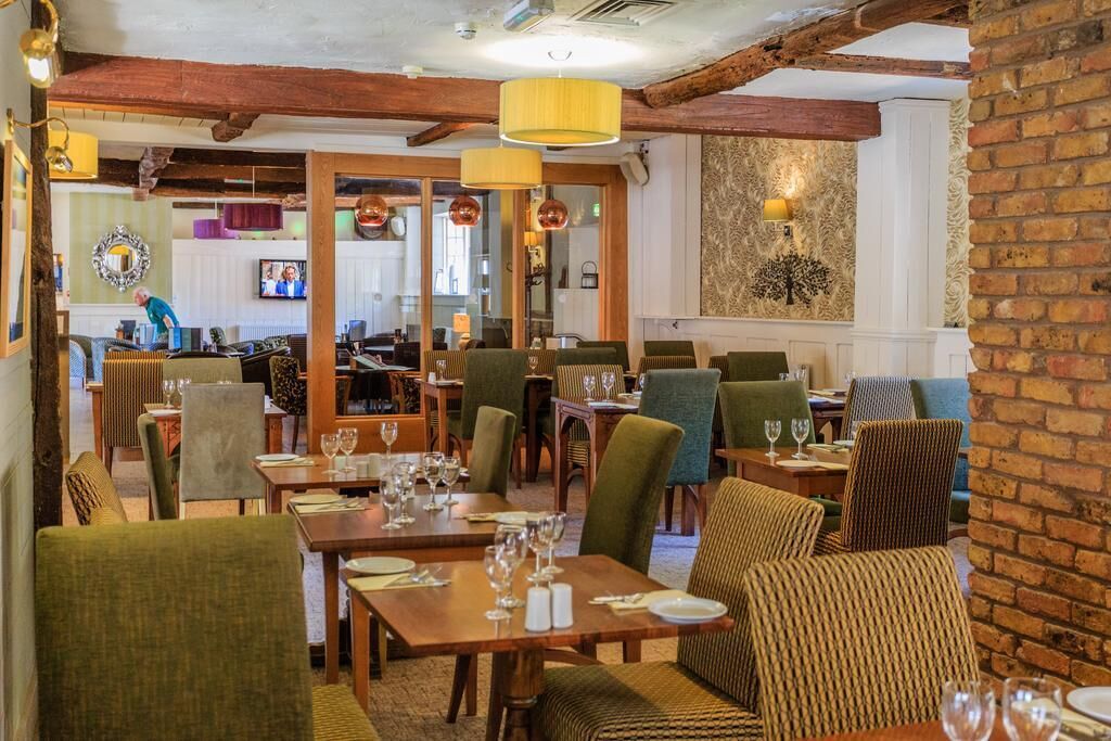 A restaurant with wooden beams, green upholstered chairs, and tables set for dining.
