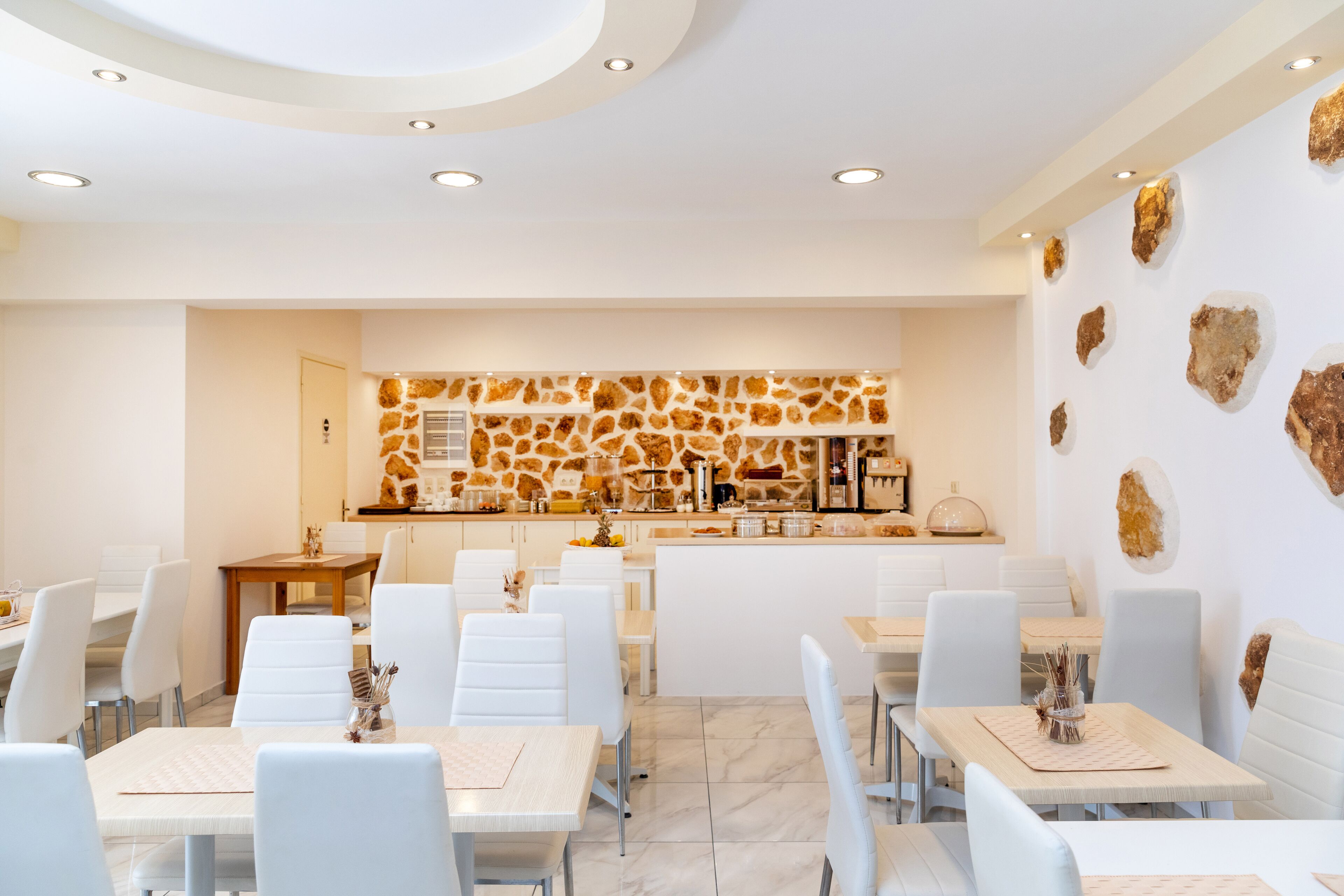 Zona pranzo moderna con sedie e tavoli bianchi, cucina con schienale in pietra e rocce decorative alle pareti.