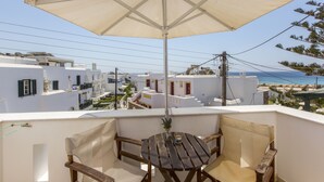 Un balcone con tavolo e sedie in legno, un ombrellone e vista sulla spiaggia e sugli edifici bianchi.