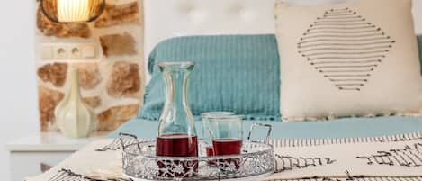 A bed with a teal blanket, a decorative pillow, and a tray with two glasses of red drink.