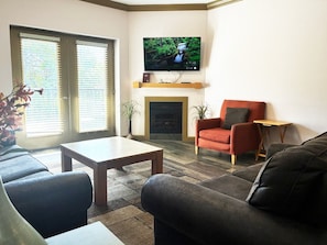 A living room with a flat-screen TV mounted above a fireplace, a sofa, a red armchair, and a coffee table.