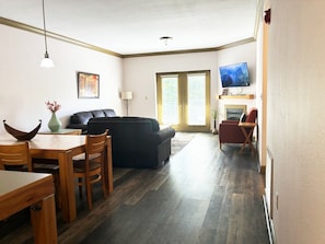 A living room with a sofa, a dining table with chairs, a TV mounted on the wall, and a fireplace.