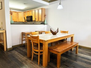 A dining area with a wooden table and chairs, a kitchen with wooden cabinets, and a hanging light fixture.