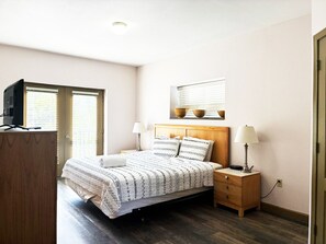 Une chambre à coucher comprenant un lit, des tables de chevet, une télévision et une fenêtre avec des stores.