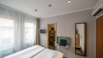 A hotel room with a bed, a desk with a laptop, a mirror, and a bathroom visible through an open door.