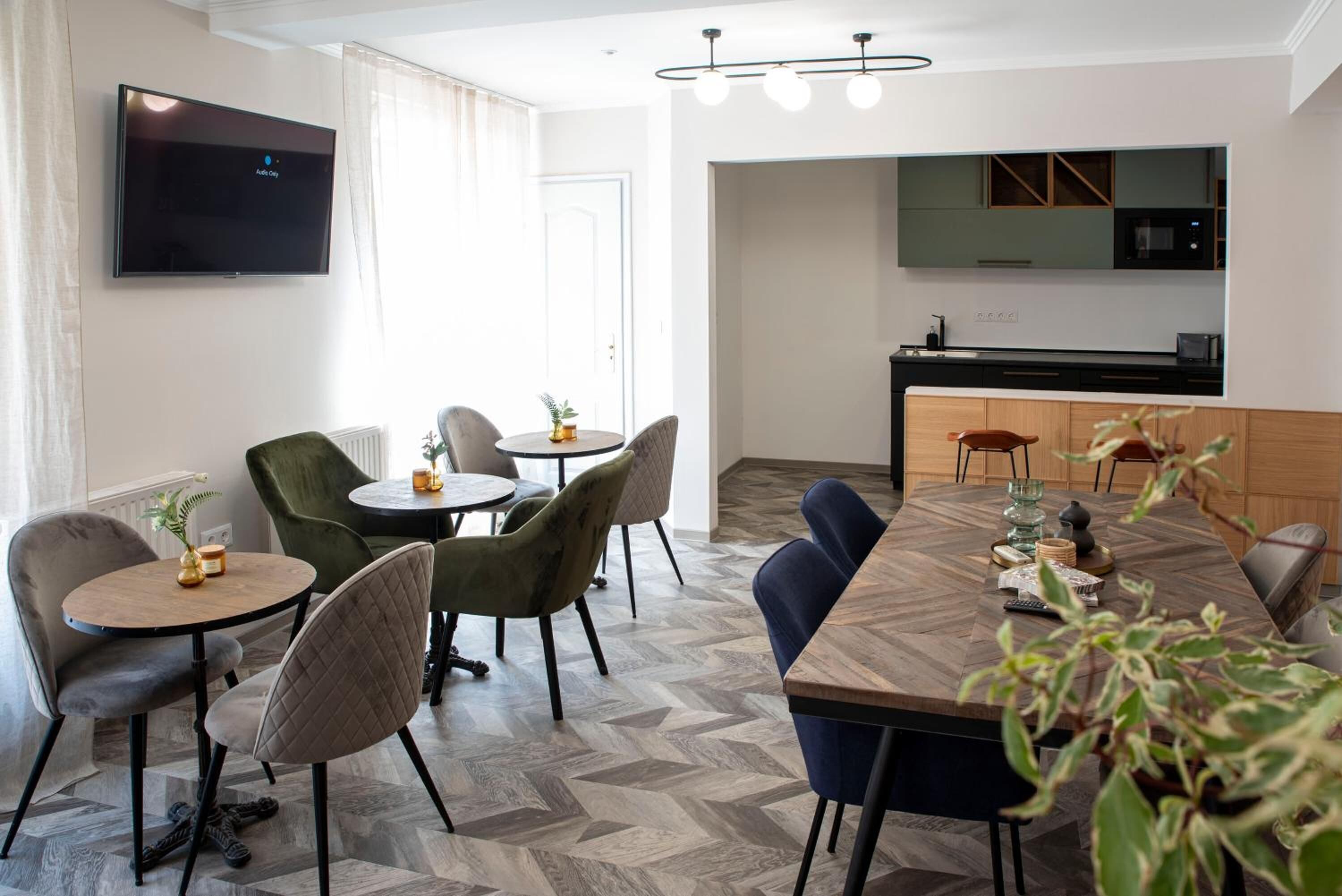 A modern hotel room with a dining area, a kitchen, and a TV mounted on the wall.