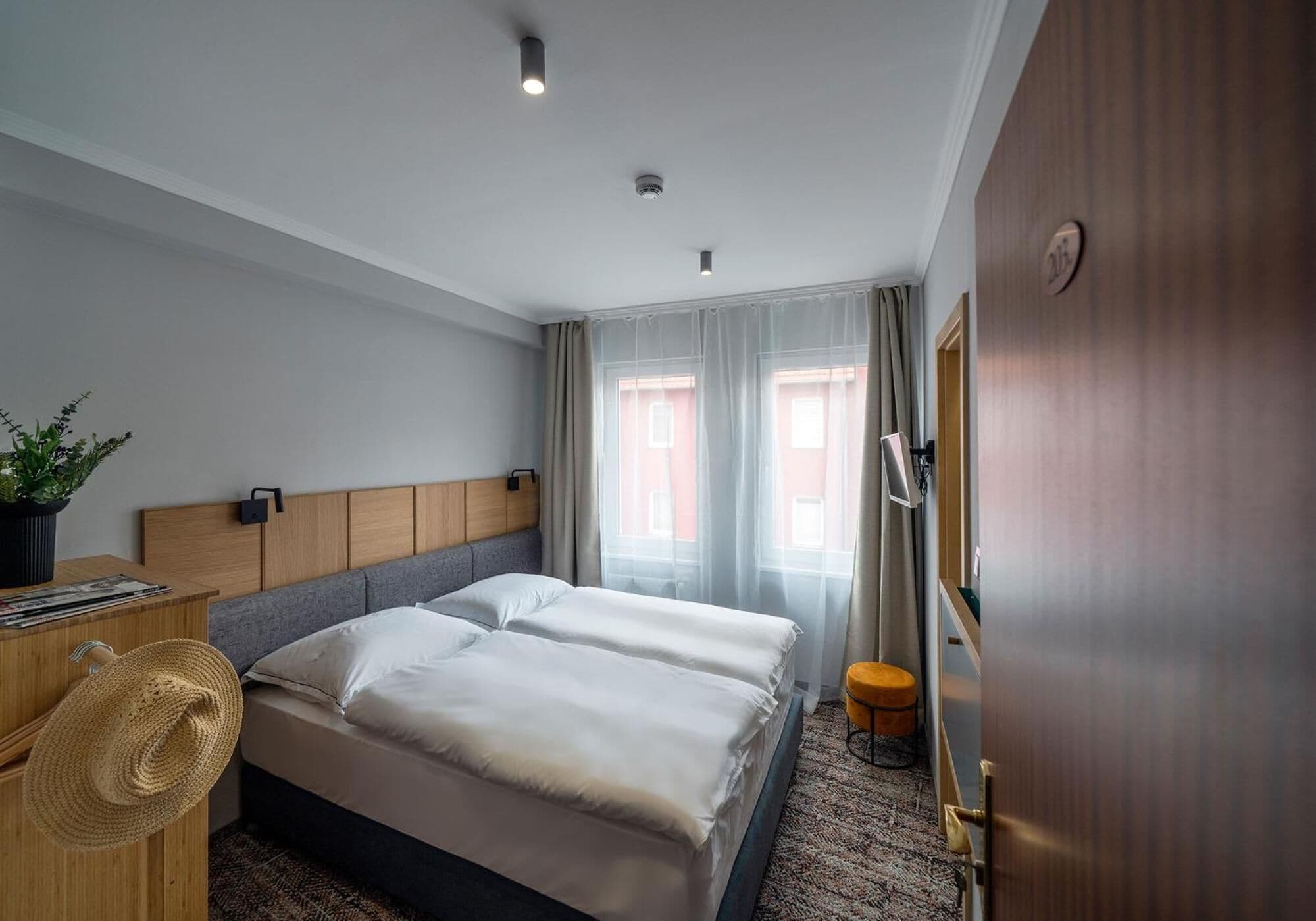 Habitación de hotel con dos camas, un cabecero de madera, un escritorio con una planta y un taburete pequeño.