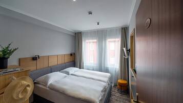 Habitación de hotel con dos camas, un cabecero de madera, un escritorio con una planta y un taburete pequeño.